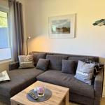 Ein Wohnzimmer mit grauem Sofa, Tisch und Fenster.