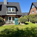 Haus mit Terrasse, Garten und Balkon unter blauem Himmel.