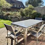 Terrasse mit metallischem Tisch und sechs Stühlen auf Pflastersteinen.