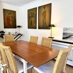 Esszimmer mit Holztisch, Rattanchairs und Wandbildern.