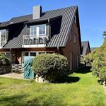 Haus mit Balkon, Garten und Steinmauer unter blauem Himmel.