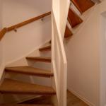 Treppenhaus mit Holzgeländer und Teppichstufen führt zur oberen Etage.