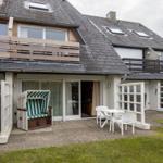 Terrasse mit Strandkorb und Tisch. Haus mit Balkon und Dachfenstern.