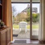 Durch Glastür zur Terrasse mit weißem Stuhl und Blick auf Gartenhaus.