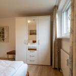 Schlafzimmer mit weißem Schrank, Fenster und Holzboden.