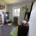 Badezimmer mit Toilette, Waschbecken und Fenster. Grün Teppiche und Pflanze.