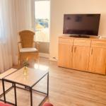 Wohnzimmer mit TV, Sitzgelegenheit und Balkontür.