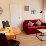 Ein Wohn- und Essbereich mit rotem Sofa, Tisch und Stühlen sowie Wandbildern.