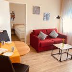 Wohnbereich mit rotem Sofa, Esstisch und Blick in Schlafzimmer.