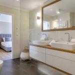 Badezimmer mit Doppelwaschbecken, Spiegel und Blick in Schlafzimmer.
