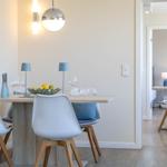 Esszimmer mit Tisch, Stühlen und Deckenleuchte. Durchgang zu weiterem Raum mit Tisch und Stuhl.