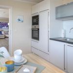 Küche mit weißen Schränken, Edelstahlspüle und Blick in Wohnzimmer.