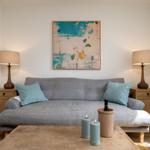 Ein grauer Sofa mit zwei Kissen, zwei Lampen und einem Bild an der Wand.