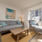 Wohnzimmer mit Sofa, Sessel und Tisch. Wandbild und große Fenster.