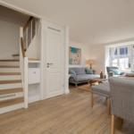 Haus mit Holzstufen, Wohnzimmer und Essbereich mit grauer Couch und Holzboden.