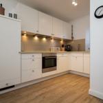 Moderne Küche mit weißen Schränken, Holzboden und integriertem Ofen.