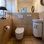 Badezimmer mit Toilette, Waschbecken und Spiegel. Holzwand und Bodenfliesen.