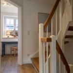 Treppenhaus mit Holzgeländer und Blick in Arbeitszimmer mit Schreibtisch.