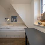 Schlafzimmer mit Dachschrägen, Bett mit Schubladen, Nachttisch und Segelbootmodell.