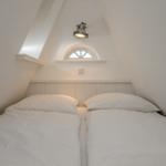 Doppelbett unter schrägen Dachschrägen mit Fenster und Deckenleuchte.