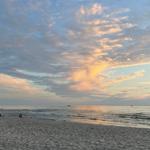 Strand bei Sonnenuntergang mit Wellen und bewölktem Himmel.