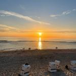Sonnenuntergang am Strand mit Strandkörben und Menschen in der Ferne.