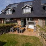 Haus mit Terrasse, Picknicktisch und Strandkorb. Schwarzes Dach, Ziegelmauer und Garten.
