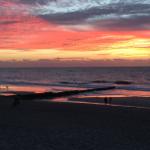 Sonnenuntergang am Strand mit Reflexion im Wasser und Silhouetten von Personen.