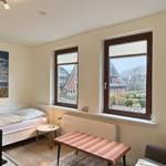 Room with bed, table, and two windows overlooking houses.
