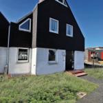 Schwarzes Haus mit weißem Sockel und Fenstern mit Vorhängen.