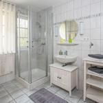 Badezimmer mit Dusche, Waschbecken und Toilette. Fenster mit Jalousie.