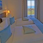 Wohnzimmer mit Sofa, Sessel und TV. Große Fensterfront mit Blick.