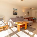 Wohnzimmer mit Sofa, Sessel und Esstisch. Gelbe Vorhänge und Holzmöbel.