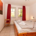 Schlafzimmer mit Doppelbett, roten Vorhängen und Holzstuhl.
