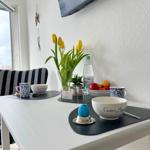 Esstisch mit Blumen, Obst und Tassen. Fernseher an der Wand.