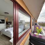 Balkon mit Stühlen und Tulpen. Blick auf Straße und Gebäude. Schlafzimmer mit Bett und Küche sichtbar.