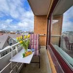Balkon mit Stuhl, Tisch und Tulpen. Blick auf Dächer und Himmel.