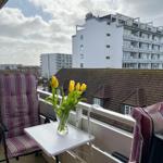 Balkon mit Stuhl, Tisch und Tulpenblumen. Blick auf Gebäude und Dächer.