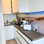 Küche mit weißen Schränken, Holzoptik Arbeitsplatte und Strandbild hinter dem Herd.