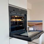 Eingebaute Dunstabzugshaube mit offenem Ofen und Brot im Backofen.