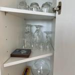 Weißer Schrank mit Gläsern und einem Glasbehälter auf den Regalen.