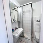 Badezimmer mit Dusche, Waschbecken und Toilette. Weiße Fliesen und Spiegelschrank.
