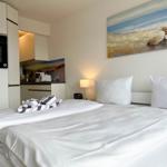 Schlafzimmer mit Bett, Nachttisch und Wandbild. Küche im Hintergrund.