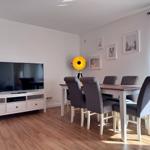 Wohn- und Essbereich mit TV, Esstisch und Stühlen. Holzboden und Wandbilder.