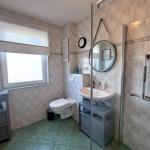 Badezimmer mit Dusche, Waschbecken und Toilette. Fenster mit Rollladen und Wanduhr.