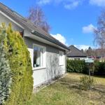 Ein Haus mit grauer Fassade, grünen Büschen und einem Garten unter blauem Himmel.