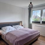 Schlafzimmer mit Doppelbett, Holzboden und Fenster mit Blick auf Außenbereich.