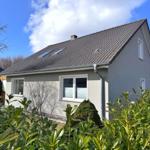 Ein Haus mit grauer Fassade, Dach mit Dachfenstern und grüner Umgebung.