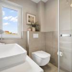 Bathroom with sink, toilet, and shower. Window with view of the sky.