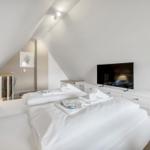 Bedroom with sloped ceiling, bed, TV, and dresser.